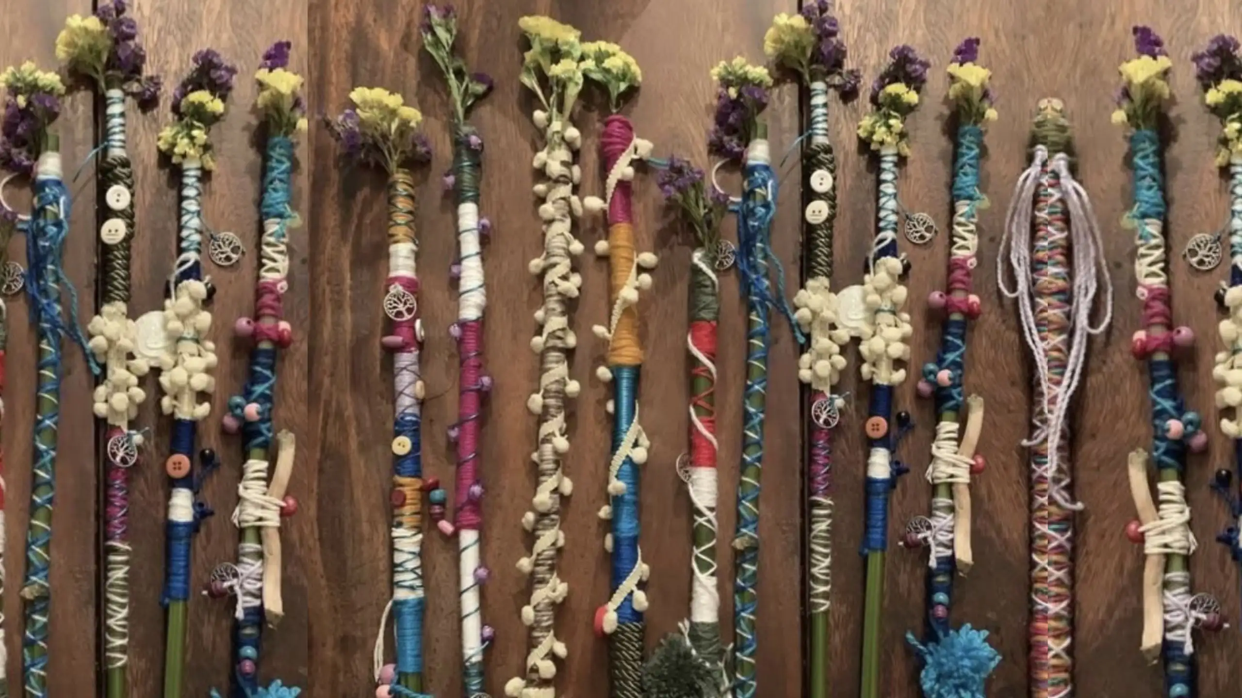 Decorative handmade magic wands wrapped in colourful threads, beads, buttons and dried flowers, arranged in rows on a wooden surface with intricate craft details.